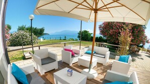 Un patio exterior con mobiliario de mimbre, un parasol grande y vista al mar.