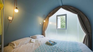 Un dormitorio con cama, ventana con cortinas e iluminación en la pared.