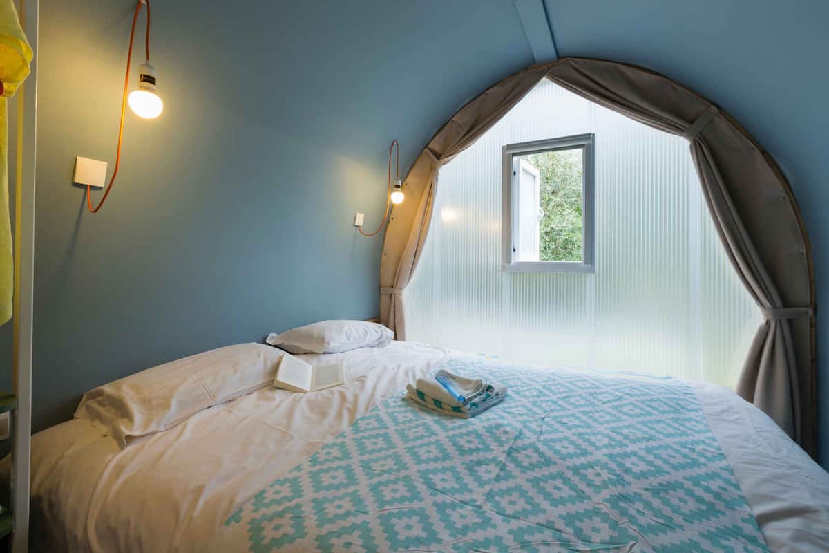 A bedroom with a bed, a window with curtains, and wall-mounted lights.