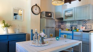 Cocina con microondas, refrigerador y armarios azules. Hay un reloj en la pared y una mesa con un mantel individual.