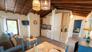 Una habitación acogedora con una mesa de comedor para cuatro personas, un sofá y una zona de cocina con armarios blancos y techo de madera.