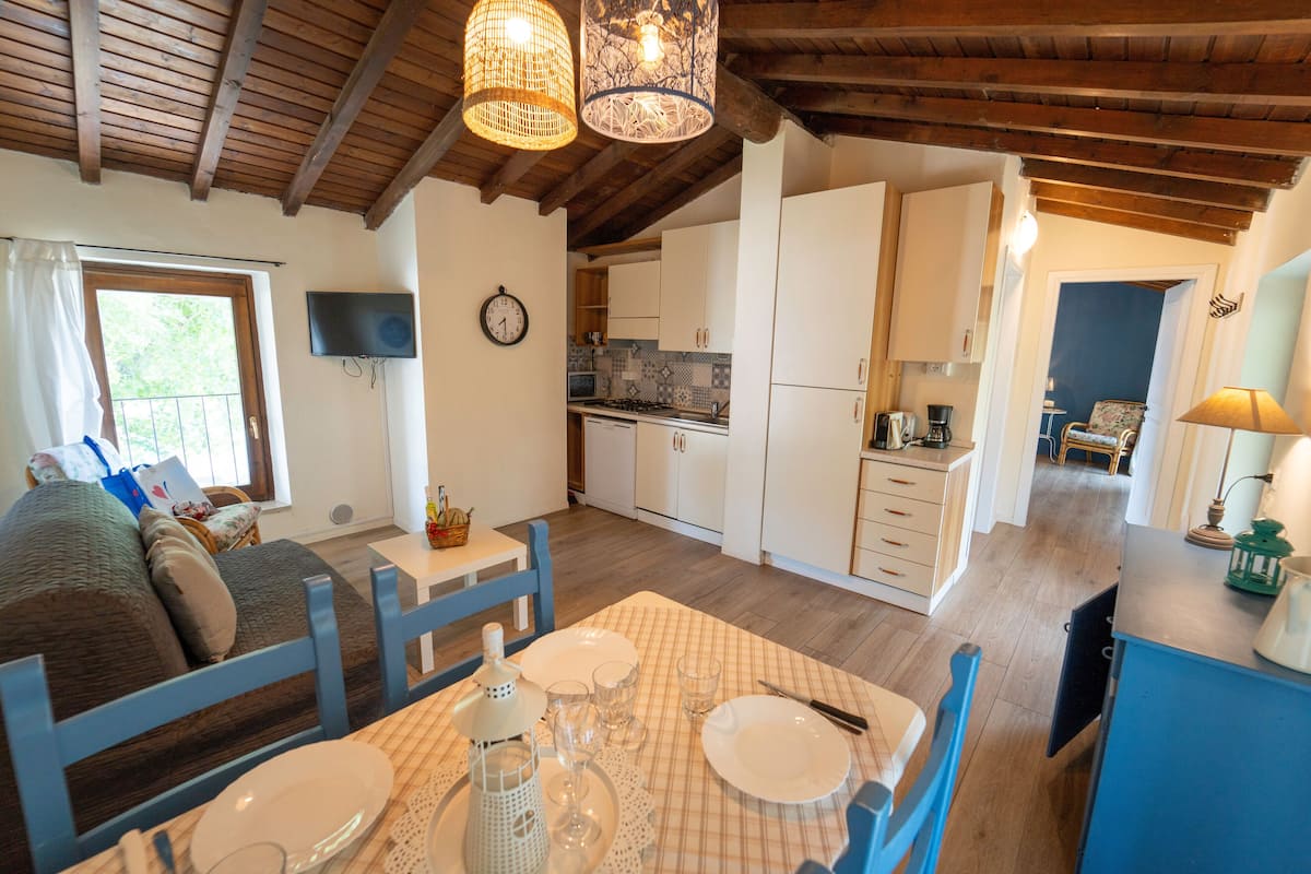 A cozy room with a dining table set for four, a sofa, and a kitchen area with white cabinets and a wooden ceiling.