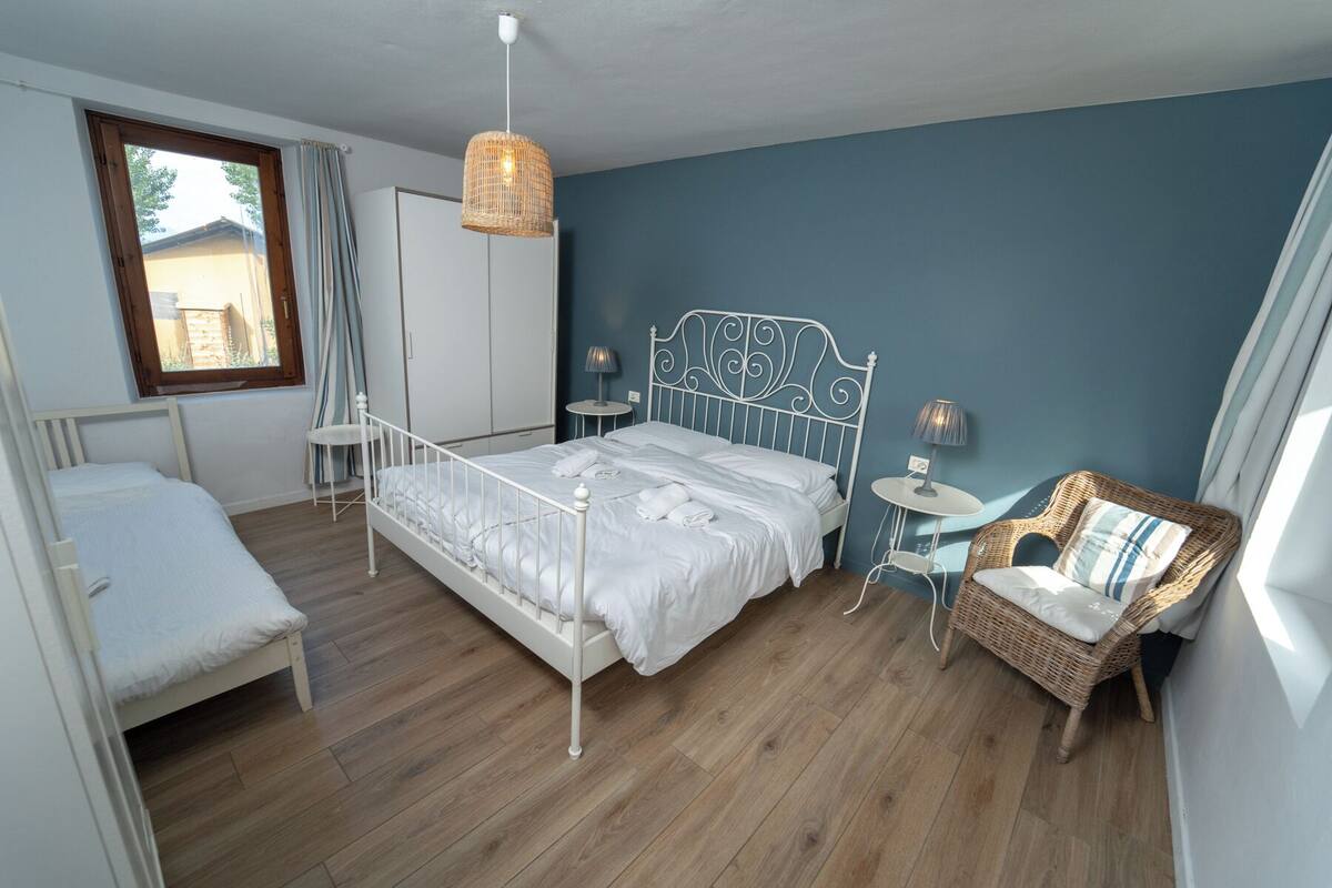 A bedroom with a bed, a chair, a small table, and a wardrobe.