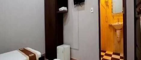 Une chambre d’hôtel avec deux lits, une armoire, un téléviseur à écran plat et une salle de bain visible à travers une porte ouverte.