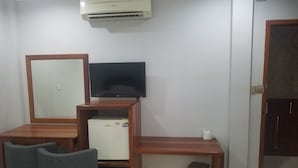 A compact room with a wooden desk, a television, a small refrigerator, two chairs, a trash bin, and an air conditioning unit. - Wei Si Deng Hotel and Restaurant (Phnom Penh)