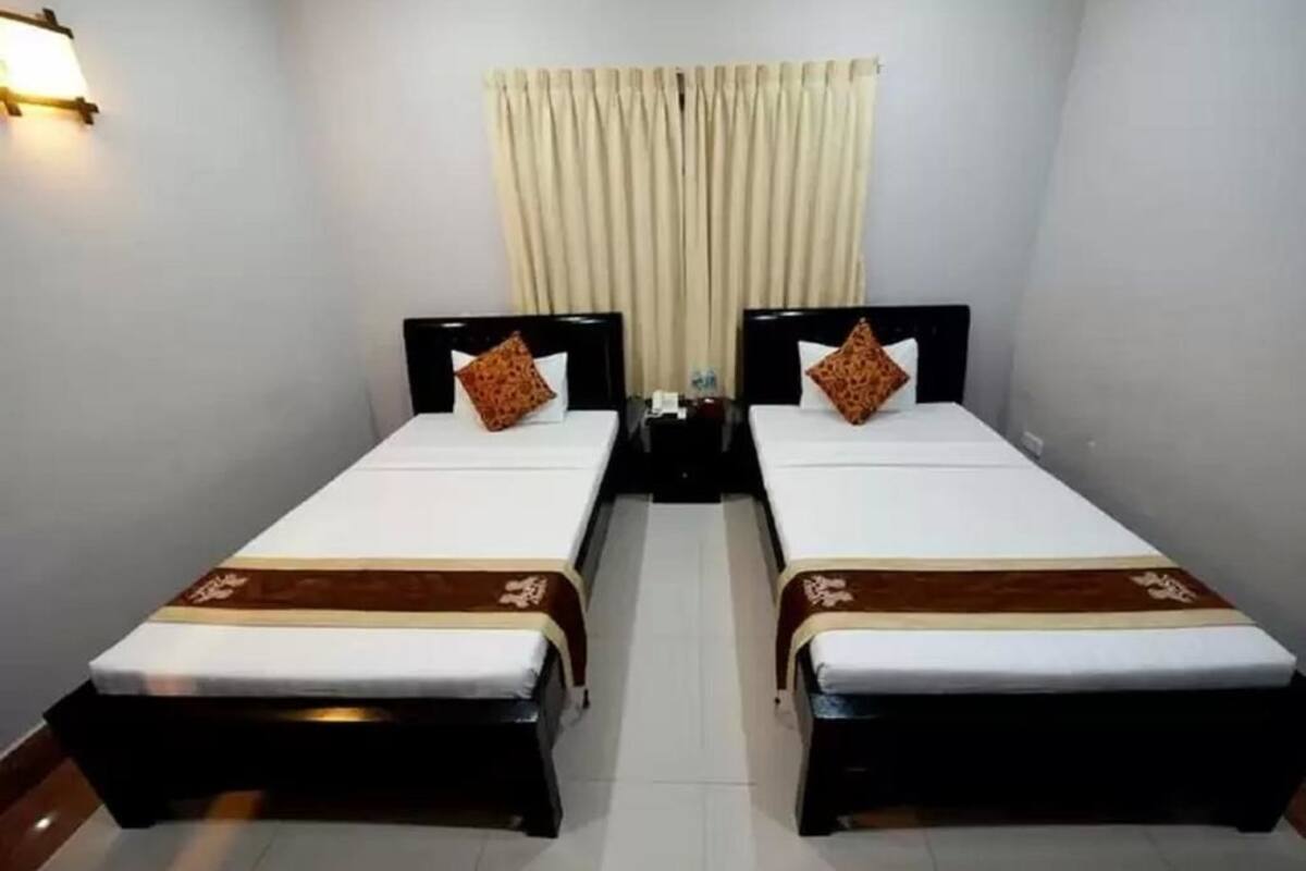 Una habitación con dos camas individuales, cada una con cabecero, mesita de noche y lámpara.