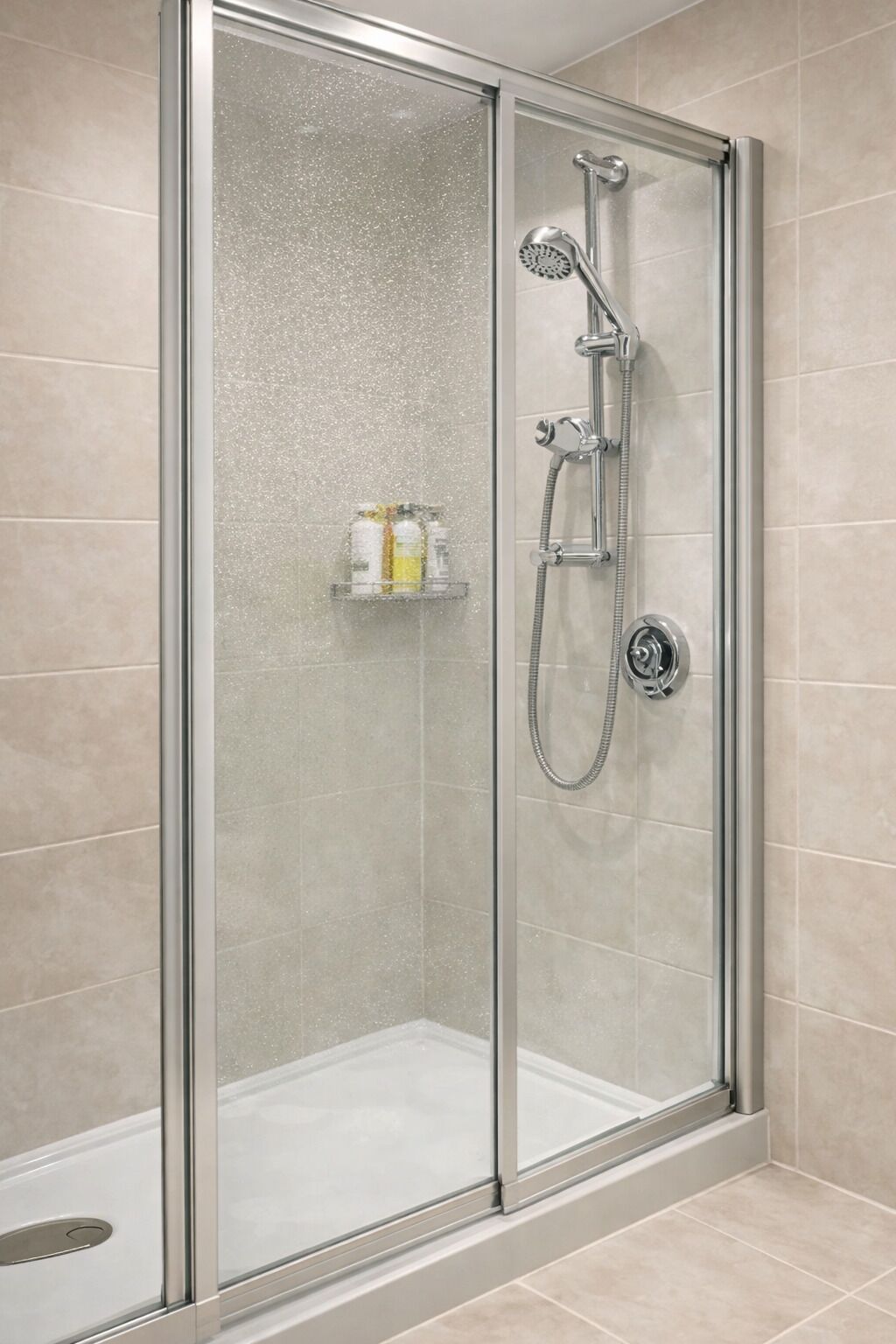 A glass-enclosed shower with a handheld showerhead and a wall-mounted faucet.