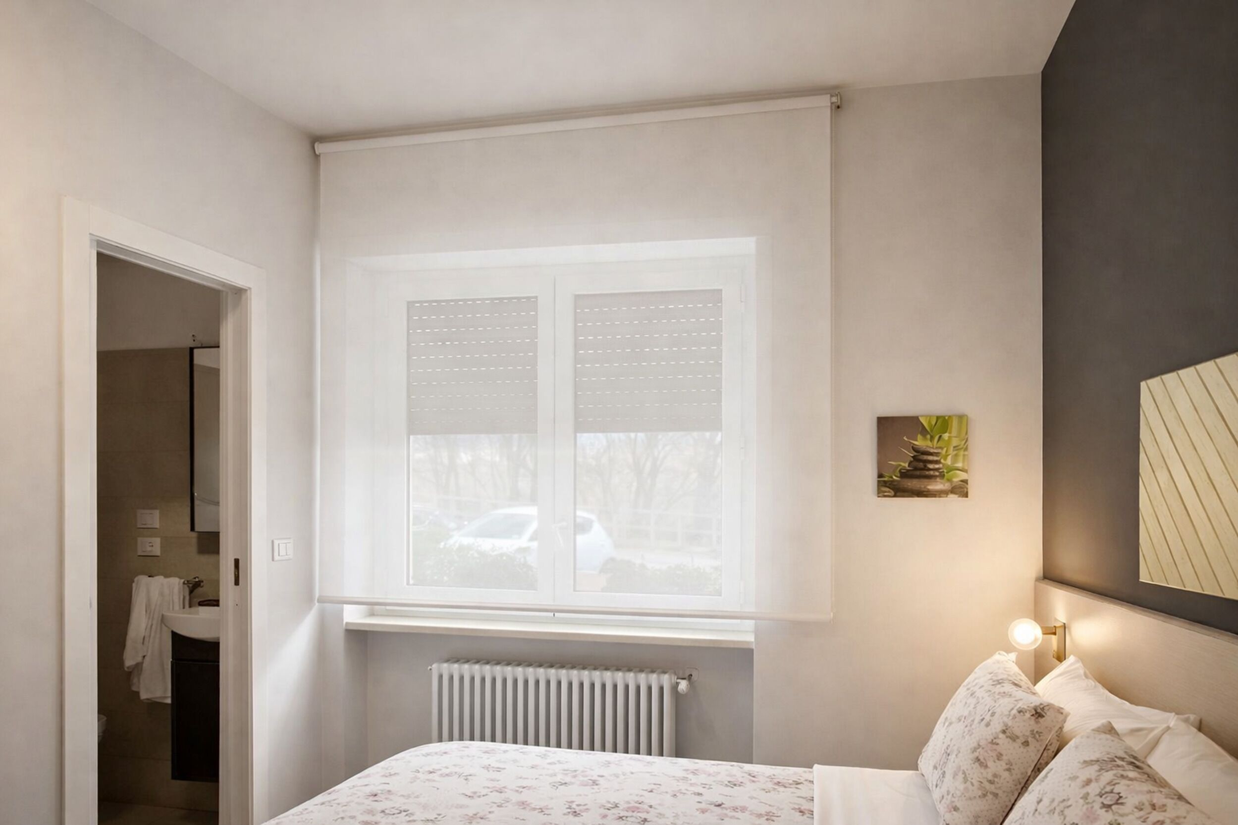 A bedroom with a bed, a window, a radiator, a nightstand, and a wall-mounted lamp.