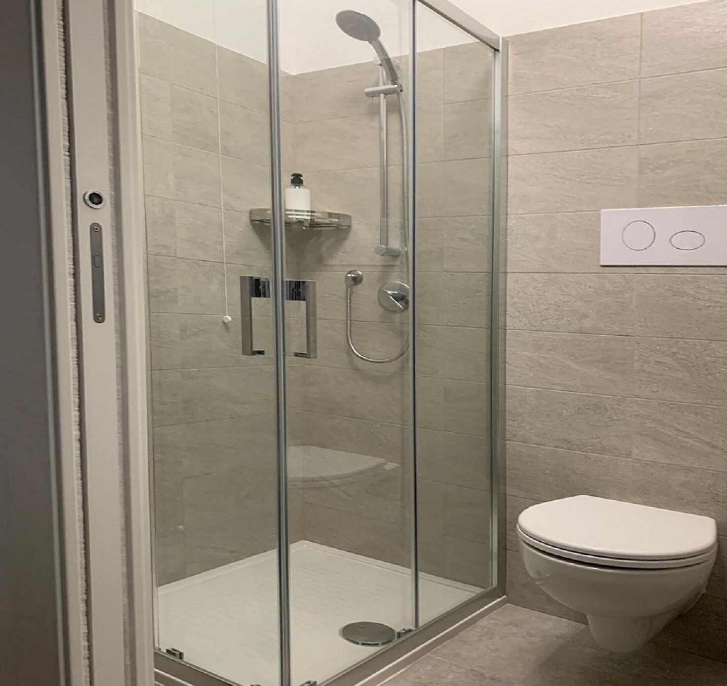 A glass-enclosed shower stall with a handheld showerhead and a wall-mounted faucet.