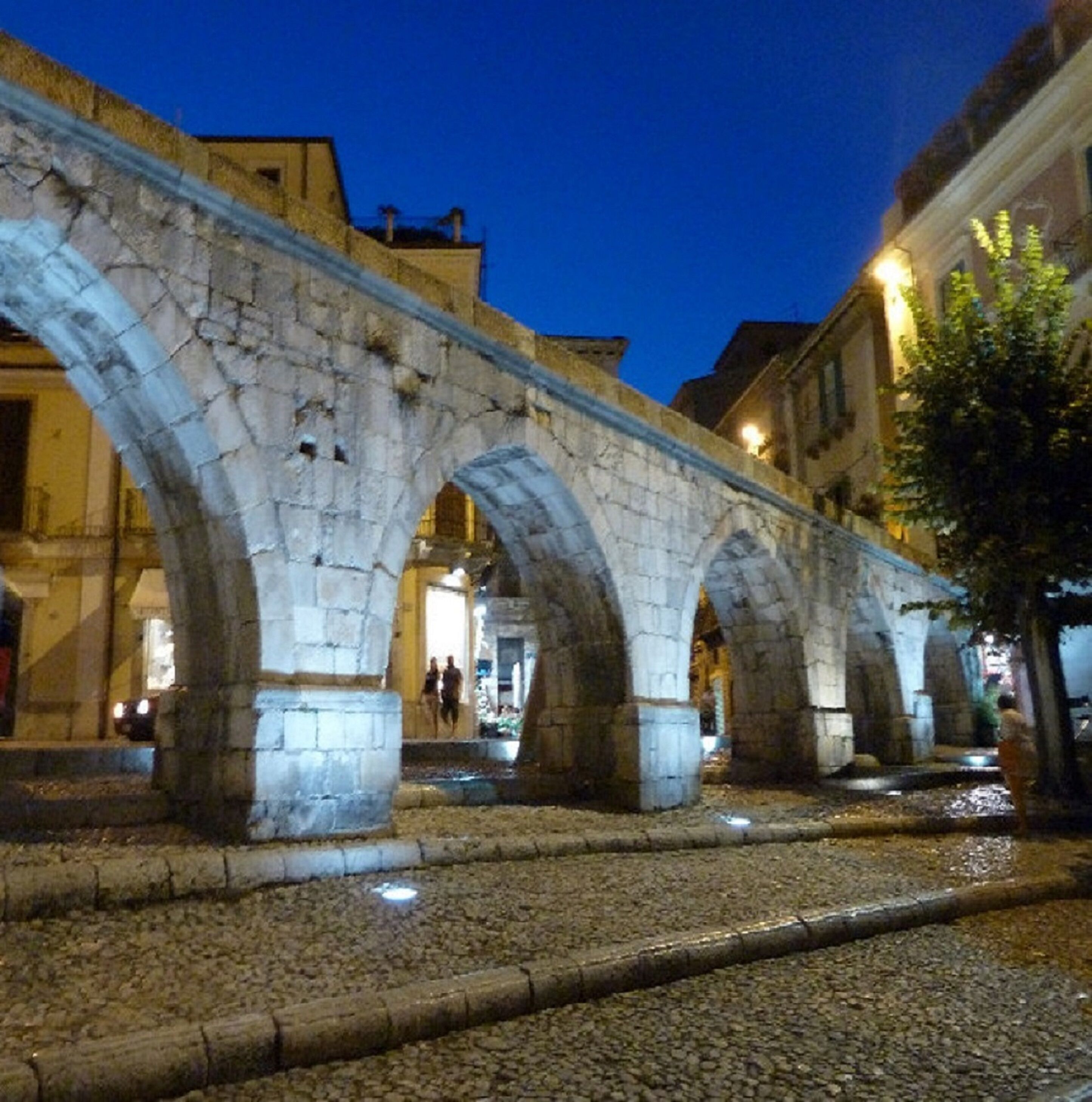 Un pont de pierre à arches multiples enjambant une rue pavée, au crépuscule.