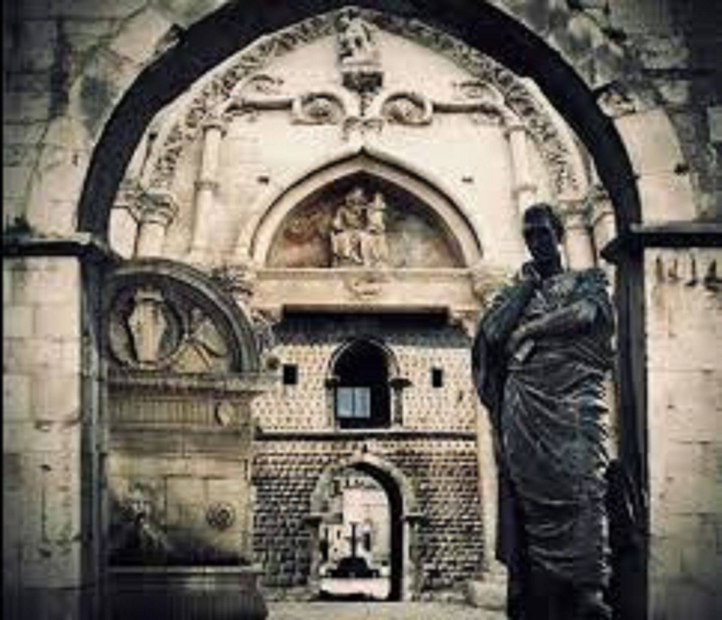 Ein historisches Gebäude mit Bogenportal, Statue und aufwendigen Steinmetzarbeiten.