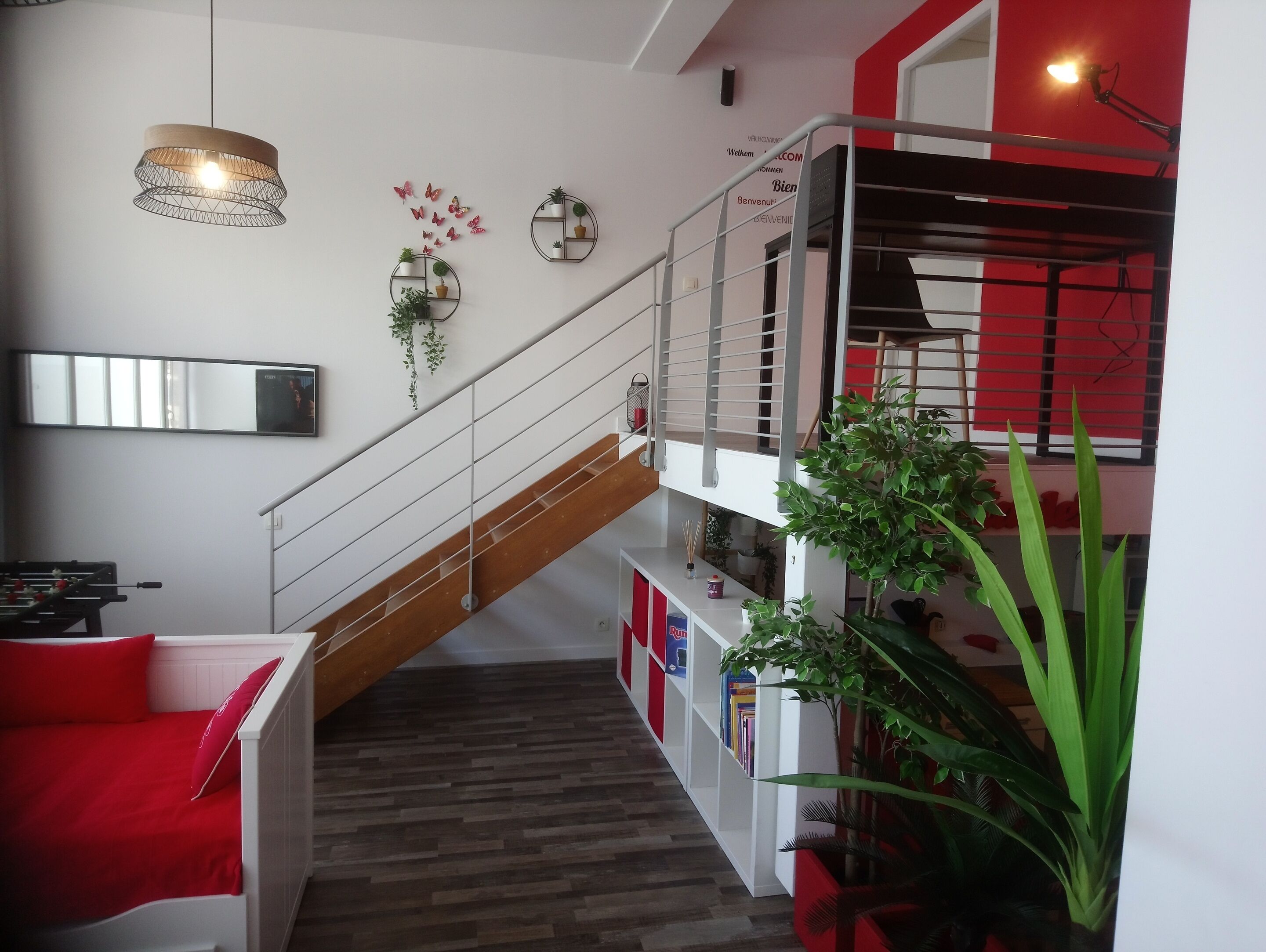 Un intérieur moderne avec un escalier, un canapé agrémenté de coussins rouges, une bibliothèque et un luminaire suspendu.