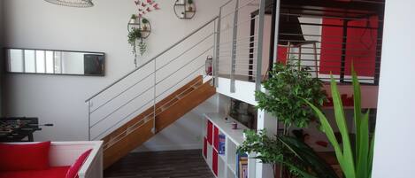 Un intérieur moderne avec un escalier, un canapé agrémenté de coussins rouges, une bibliothèque et un luminaire suspendu.