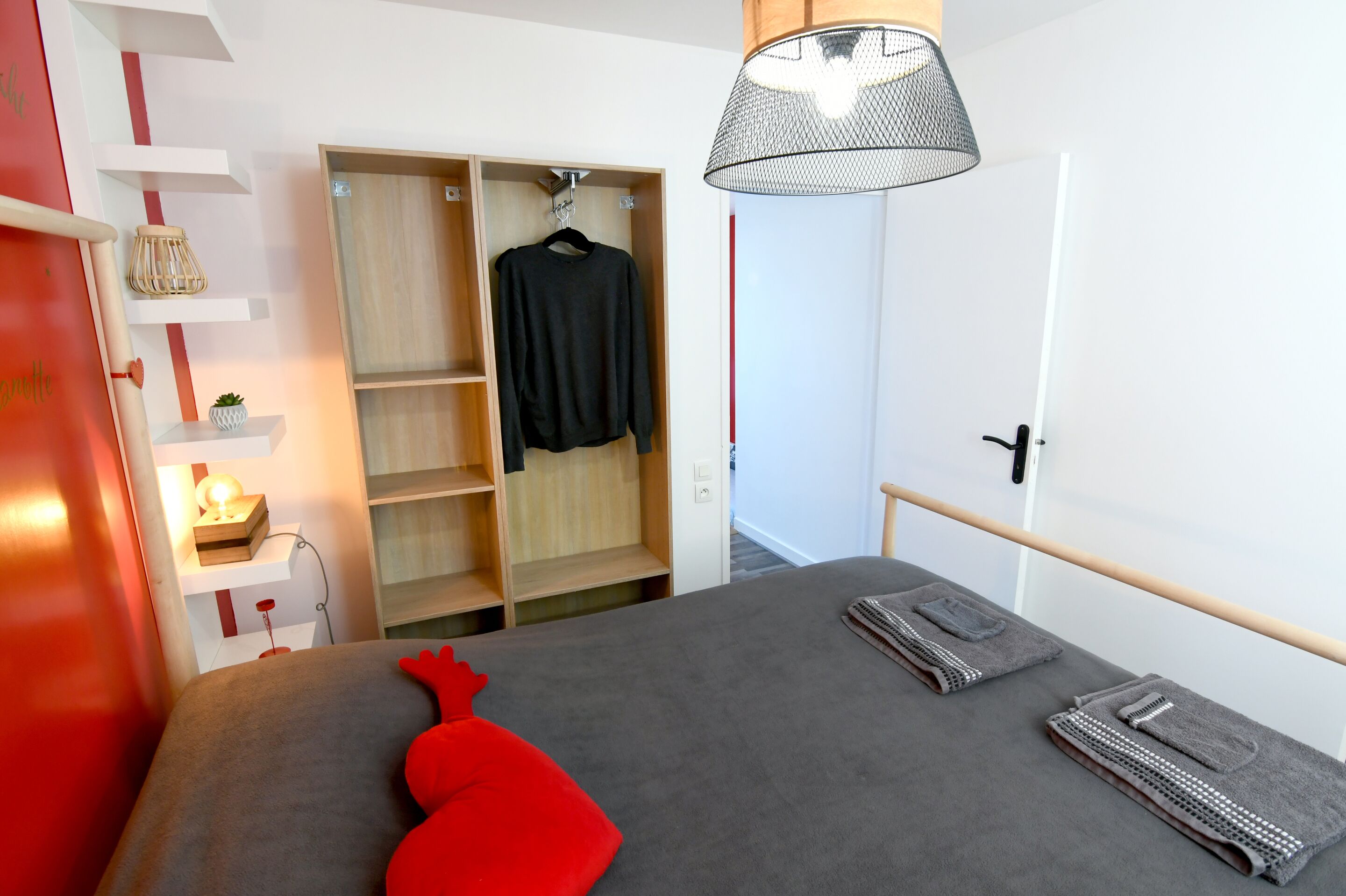 Ein Schlafzimmer mit einem Bett, einem Schrank, einer Nachttischlampe und einem roten Kissen.