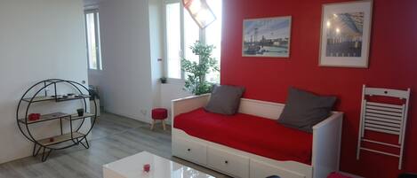 A modern living room with a red sofa, white coffee table, and a dining area with a red tablecloth.