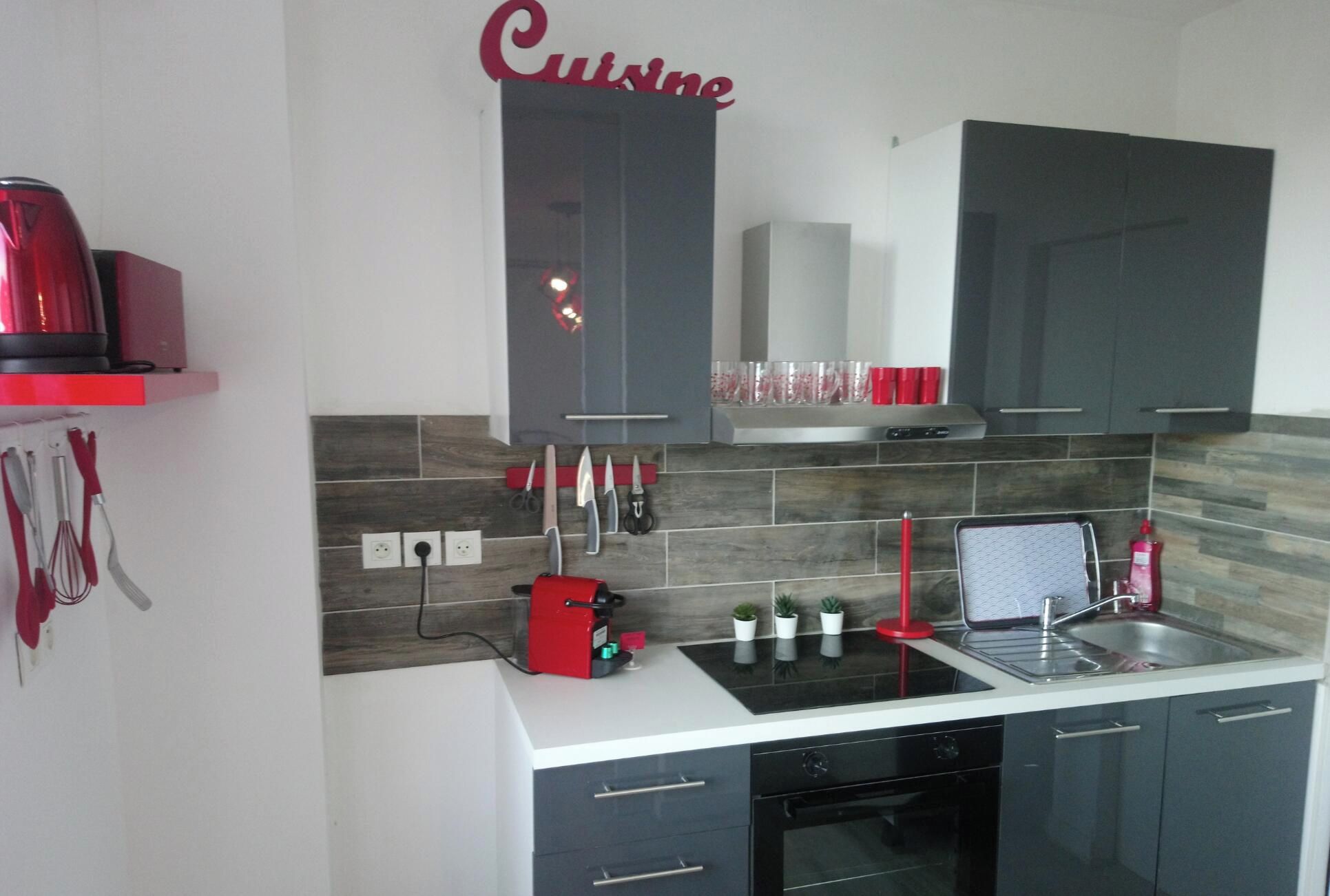 A modern kitchen with grey cabinets, a red kettle, and a countertop with various kitchen items.