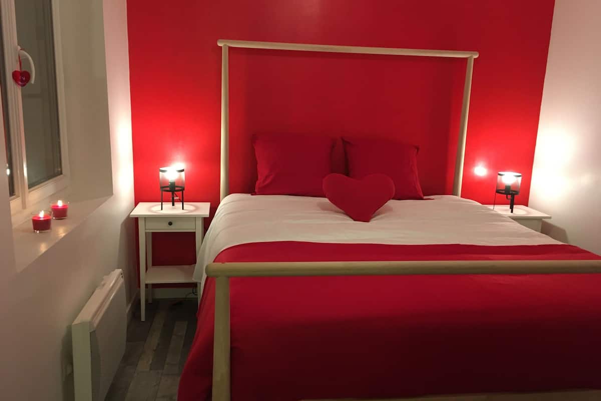 A red-themed bedroom with a four-poster bed, bedside lamps, and a window with a view.