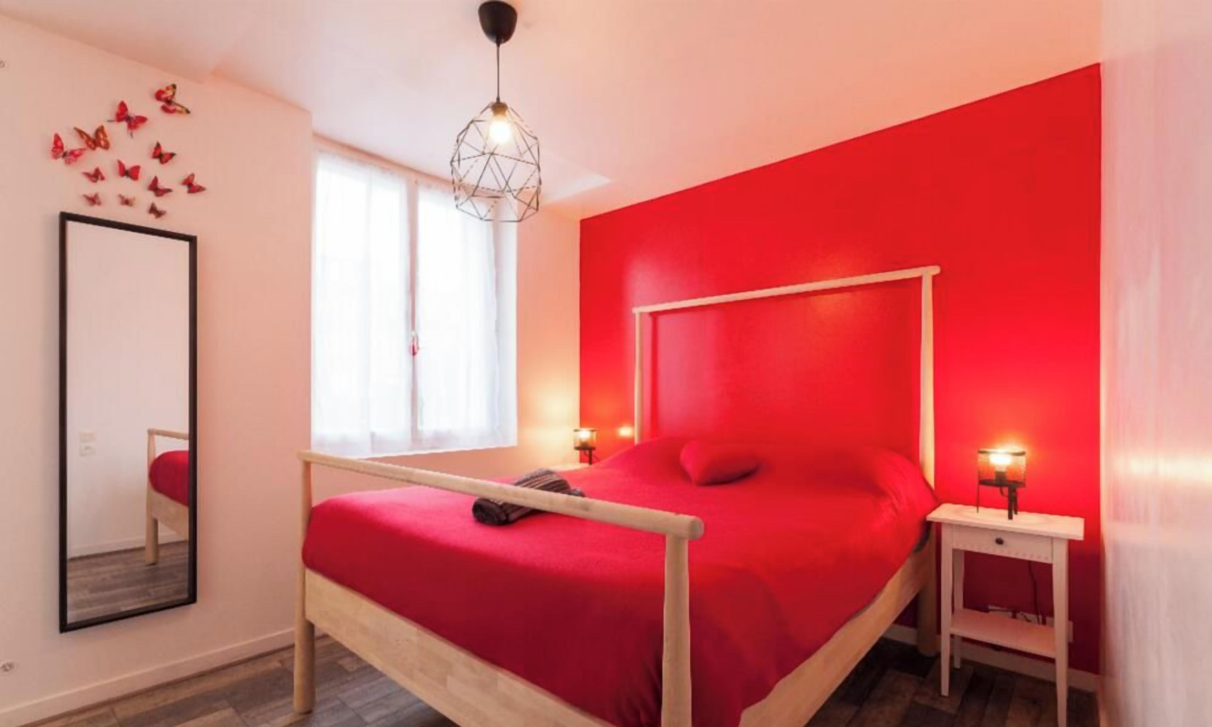 A bedroom with a bed, a bedside table, a mirror, and a window.