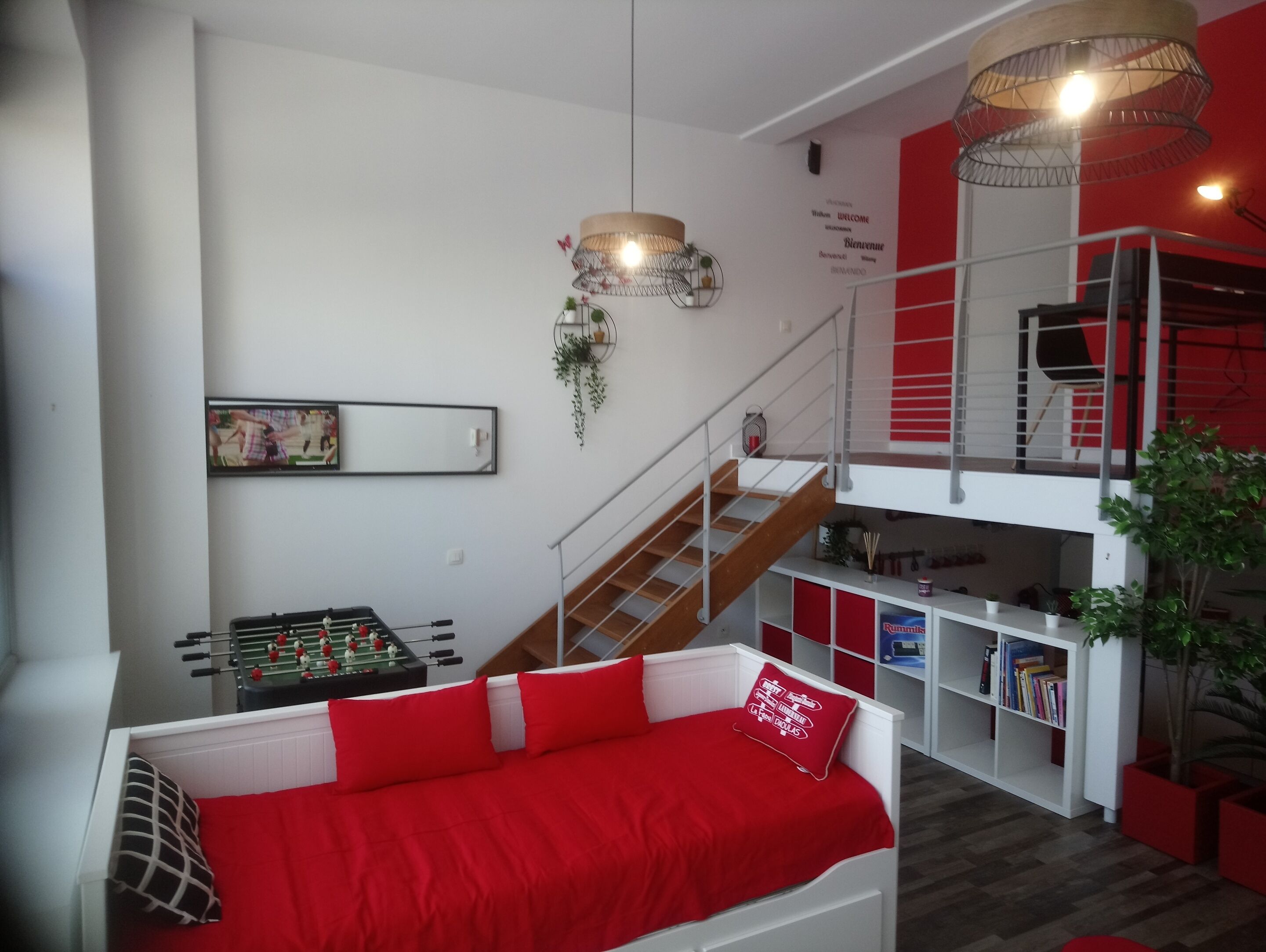 Una sala de estar moderna con un sofá rojo, una mesa de futbolín, una escalera y una estantería.