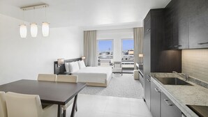 A hotel room with a bed, a desk, a chair, a dining table, a kitchen area, and a view of the city. - Hyatt Place Dubai Jumeirah Residences (Dubai)