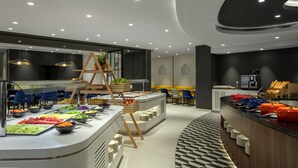 A modern breakfast buffet with various food items, a seating area with blue chairs, and a counter with kitchen appliances. - Hyatt Place Dubai Jumeirah Residences (Dubai)