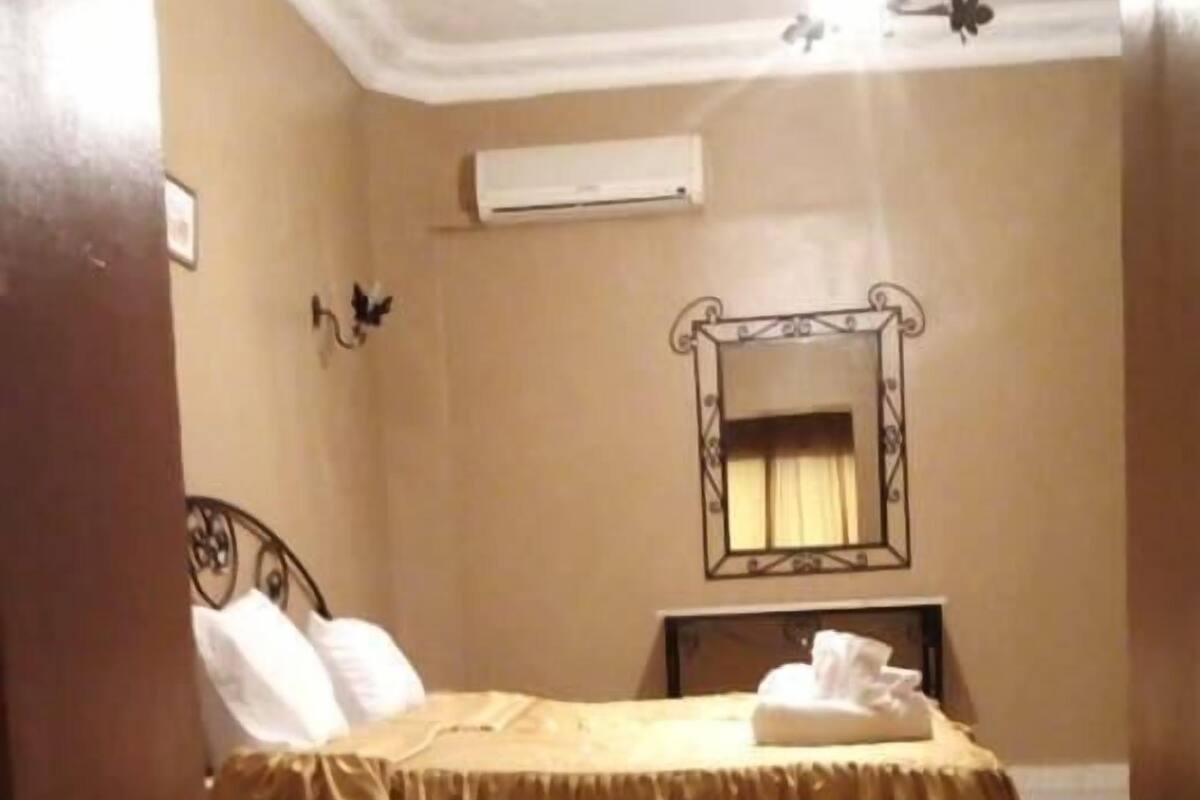 A bedroom with a bed, a bedside table, a mirror, and a ceiling fan.