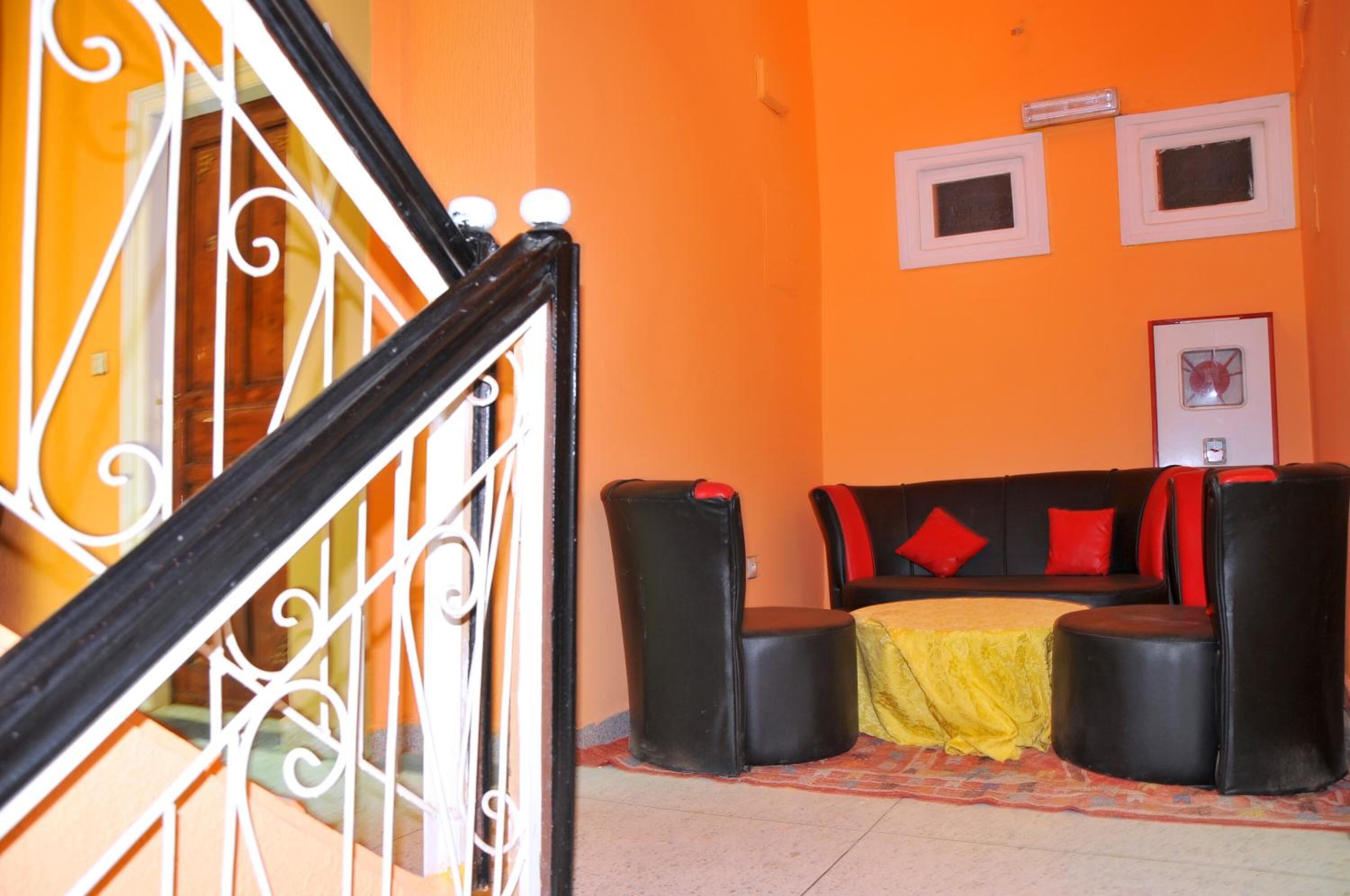 A staircase with ornate white railings, a black leather sofa with red cushions, and a yellow tablecloth on the floor.
