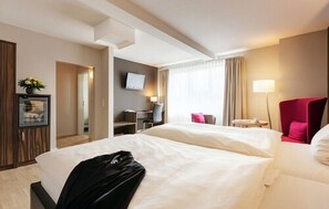 A hotel room with two beds, a desk, a chair, a TV, and a lamp. - Hotel Hiemann (Leipzig)