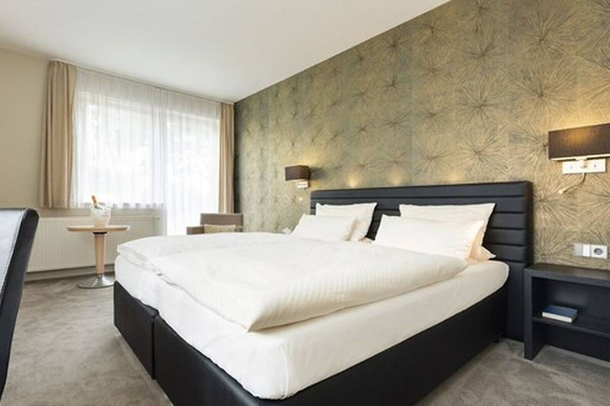 Quarto de hotel com uma cama grande, uma mesinha e uma cadeira.