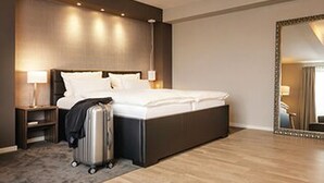 Een moderne hotelkamer met een groot bed, een nachtkastje, een lamp en een koffer.