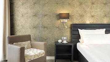 A hotel room with a bed, a chair, a nightstand, and a wall with a textured pattern.