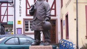 Una statua di un uomo che tiene un sacco su un piedistallo di pietra, di fronte a un edificio con una targa che indica 
