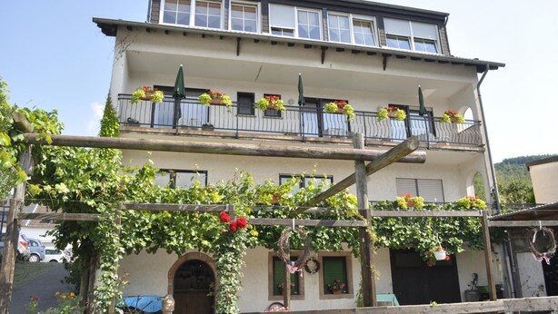 Un edificio a due piani con balconi decorati da fioriere, una recinzione di legno e un arco ricoperto d'edera.