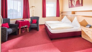 Una habitación de hotel con cama, dos sillas, una mesa y una lámpara.