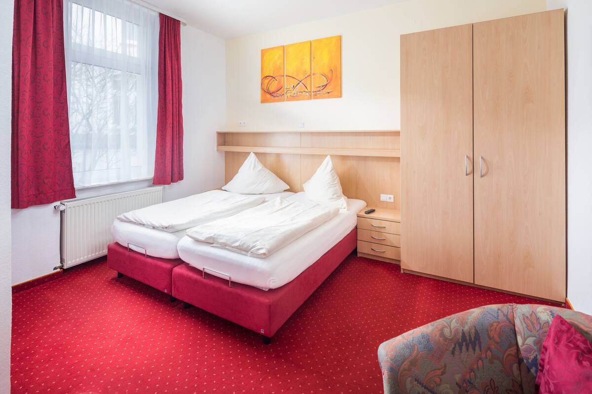 A hotel room with a bed, a nightstand, a wardrobe, and a window with curtains.