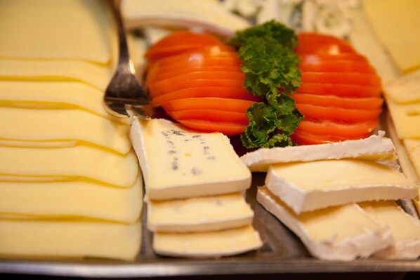 A cheese platter with various types of cheese and tomato slices. - Gästehaus Bakker (Norderney)