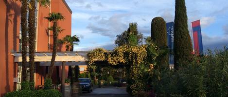 A hotel entrance with a covered walkway, palm trees, and a car parked in front.