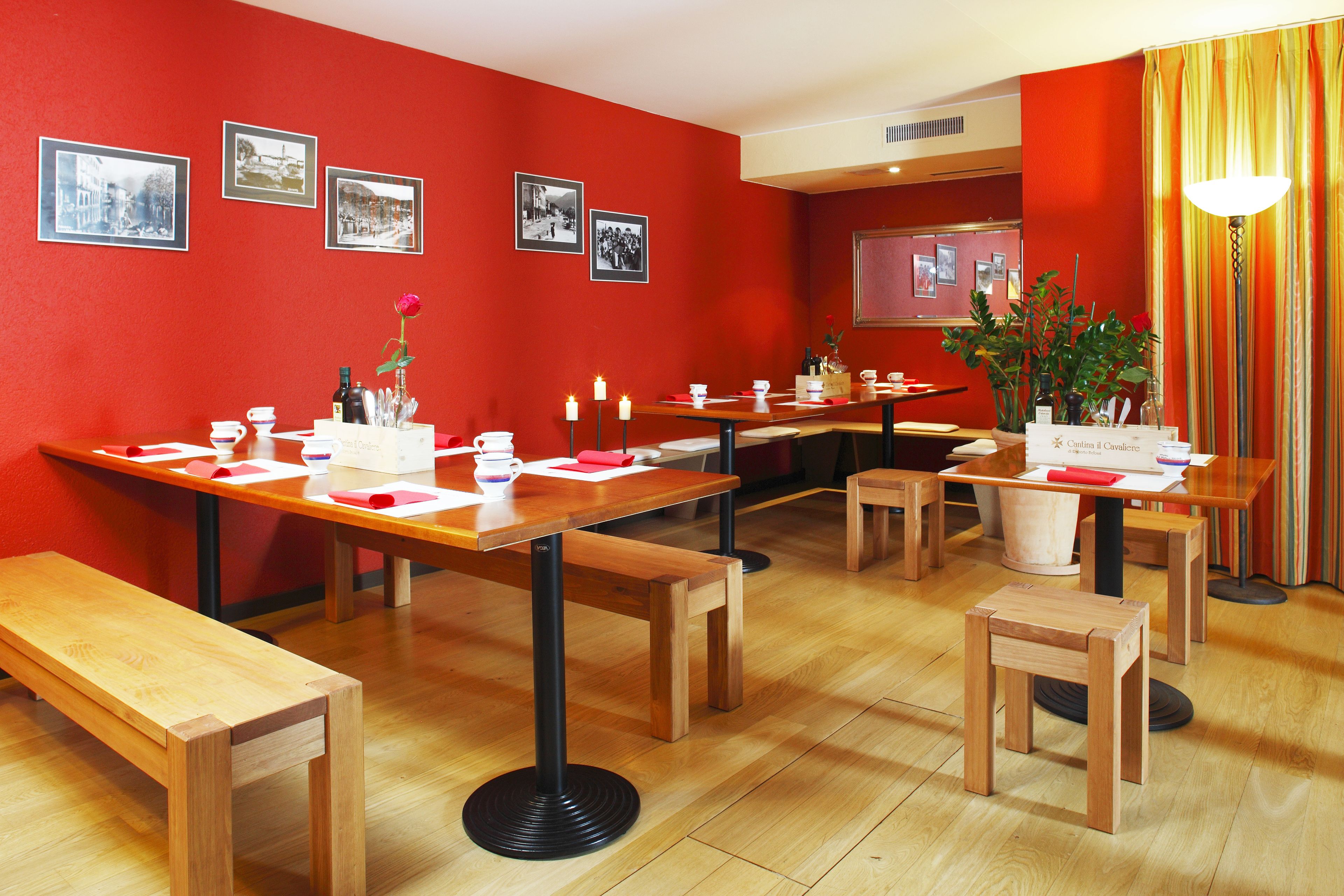 Un espace repas avec des tables et des bancs en bois, des murs rouges et des photographies en noir et blanc.