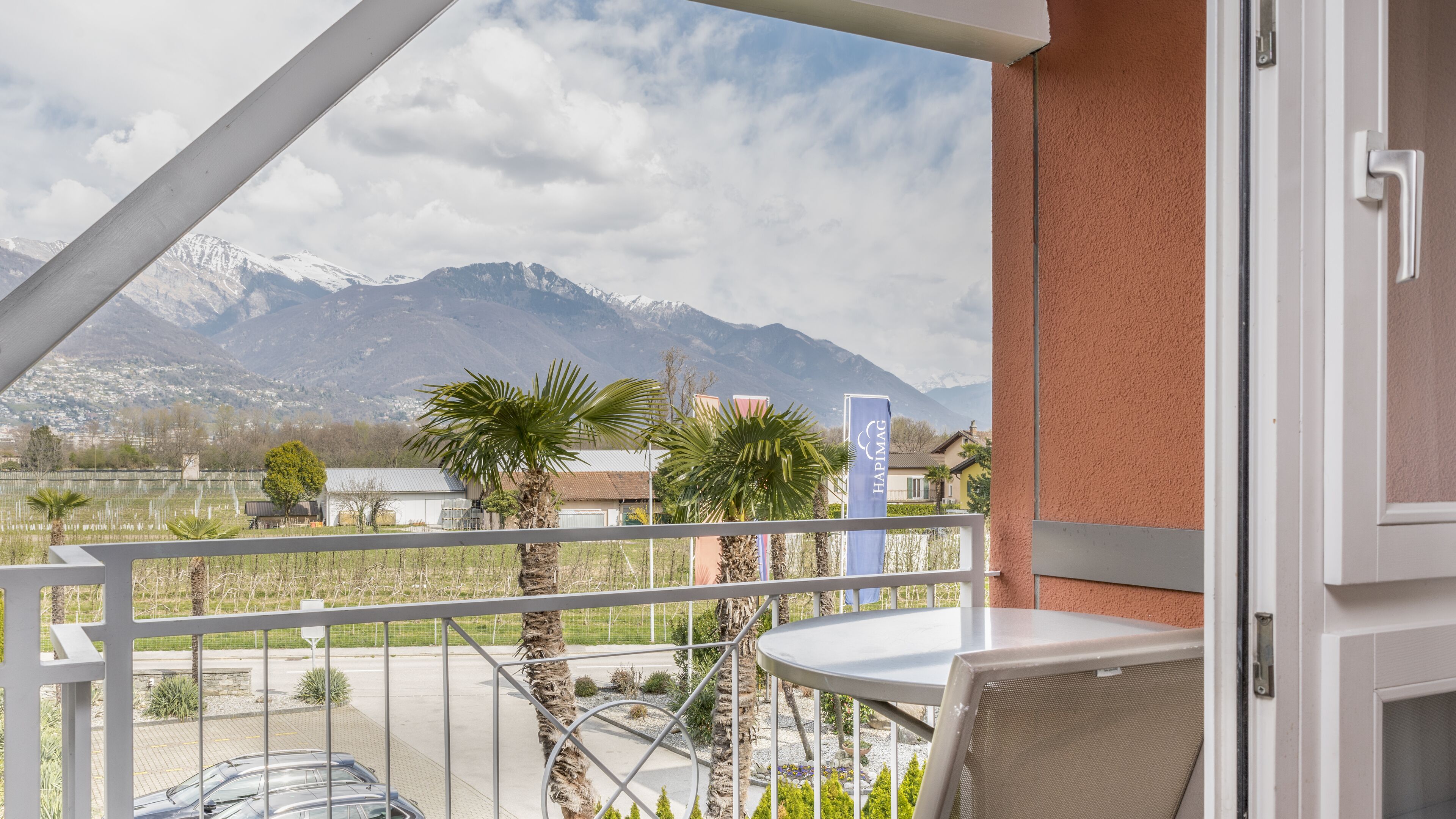 A balcony with a table and chairs, a view of mountains, and a sign for 'HAPIMAG'.
