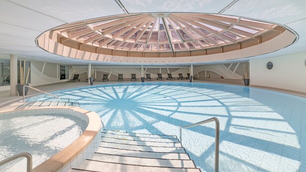 A modern indoor swimming pool with a central sunroof and a circular seating area. - Hapimag Resort Ascona (Ascona)