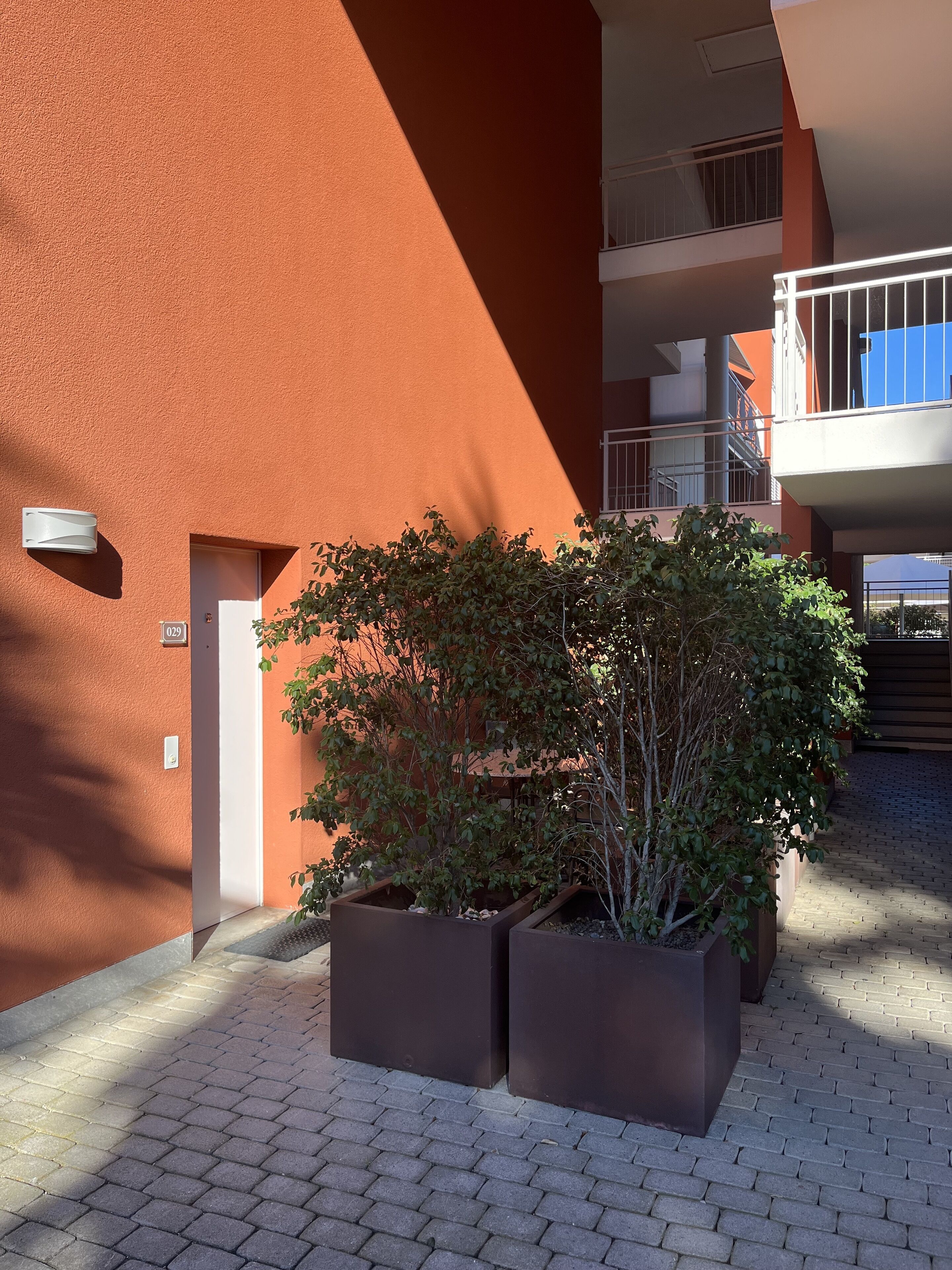 Ein Gebäude mit roter Fassade, einer Tür und einem kleinen Gartenbereich mit Blumentöpfen.