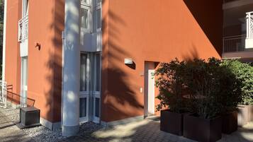 Ein modernes Gebäude mit roter Fassade, großen Fenstern und einem gepflasterten Eingangsbereich mit Pflanzenkübeln.