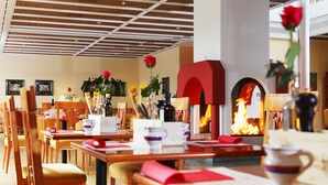 A restaurant with wooden tables and chairs, a fireplace with a visible fire, and framed pictures on the walls. - Hapimag Resort Ascona (Ascona)