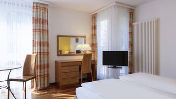 Une chambre d’hôtel comprenant un lit, un bureau avec une chaise, une télévision, une commode et une fenêtre avec des rideaux.