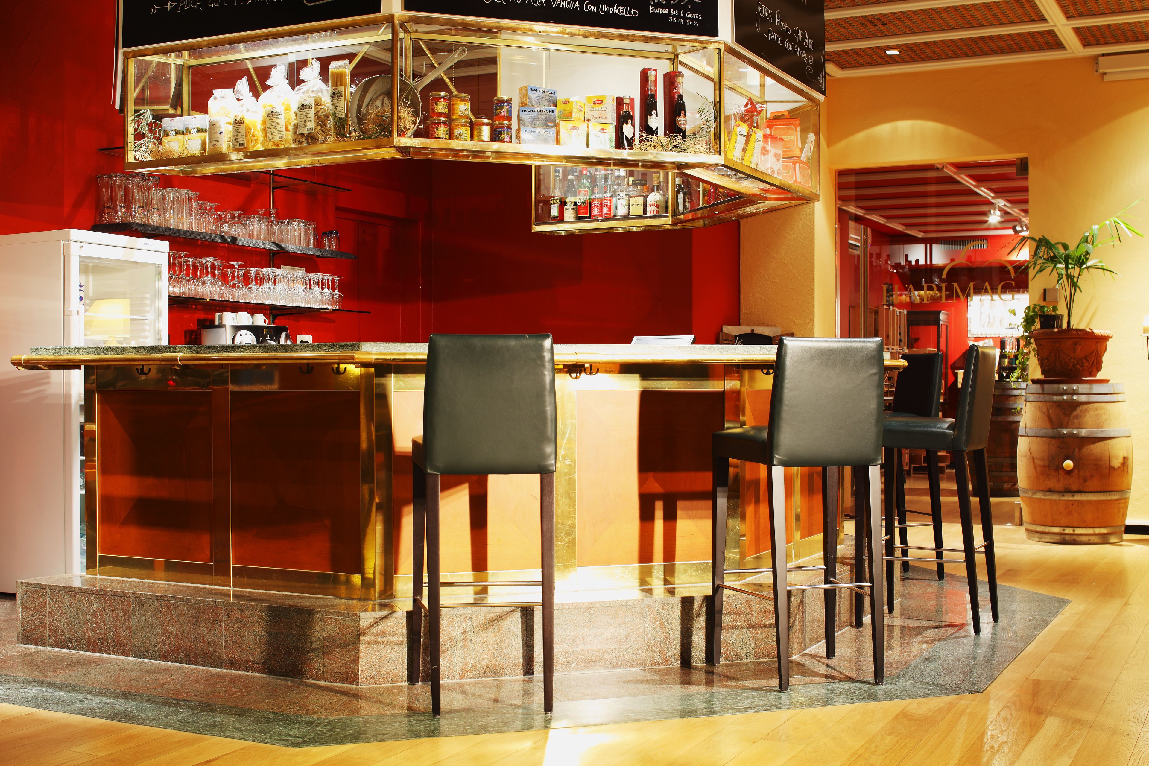 A bar area with a counter, chairs, and shelves with bottles and glasses.