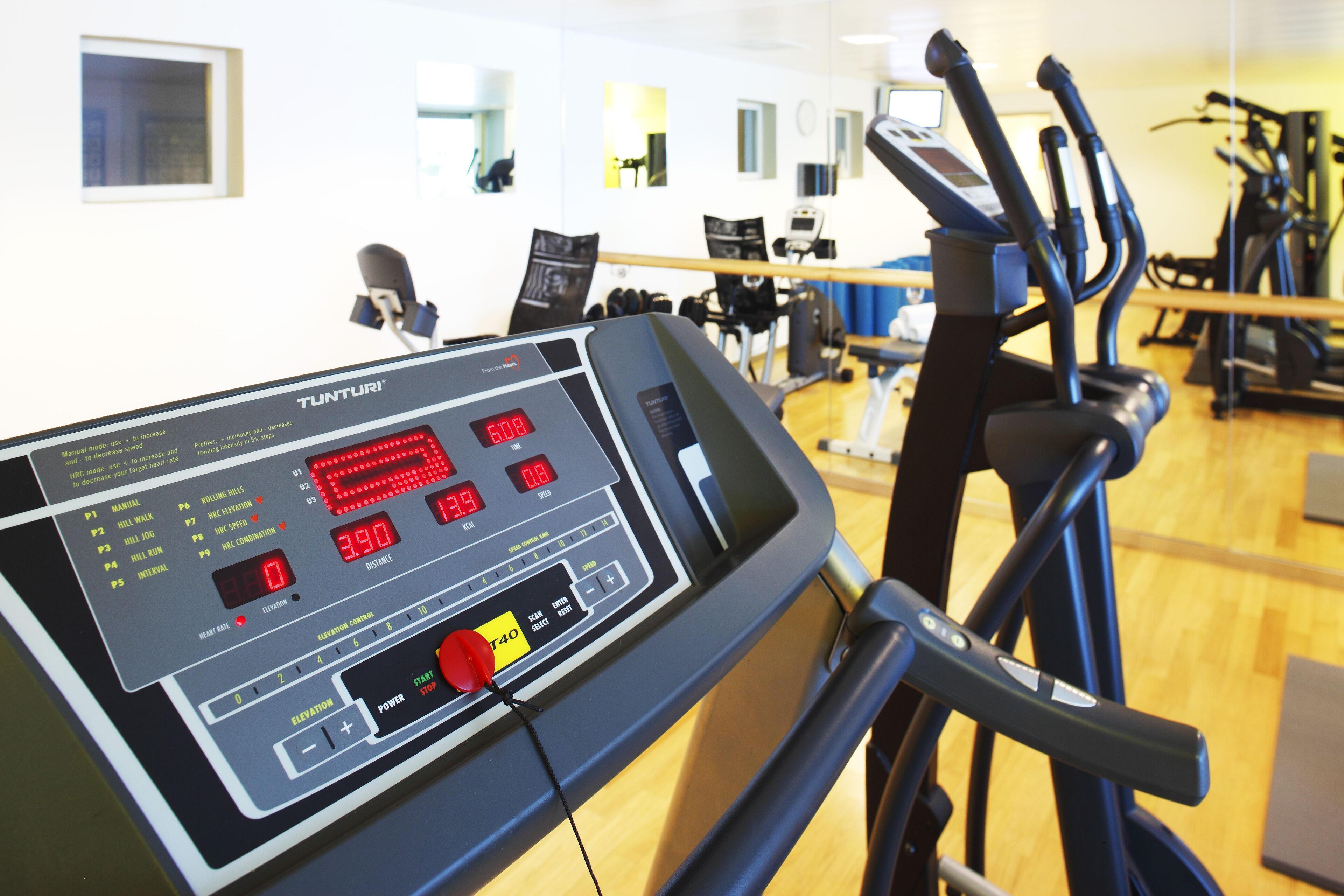A Tunturi treadmill with digital displays and control buttons, located in a gym with exercise equipment and mirrors on the wall.