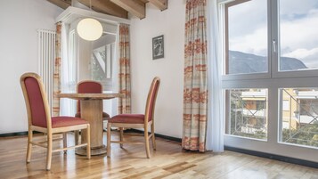Un comedor con una mesa redonda y cuatro sillas, ventanas amplias con cortinas y vistas a edificios y montañas.
