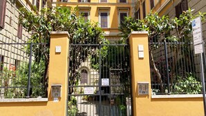 A yellow building with a gated entrance, a sign indicating a parking fee, and a sign for an introductory course. - Sweet Dream Roma Termini (Rome)