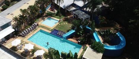 A swimming pool with a slide, lounge chairs, and palm trees.
