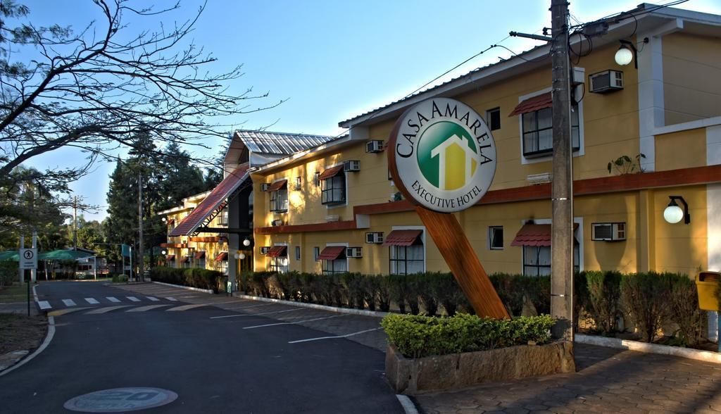 The exterior of Casa Amarella Executive Hotel with a prominent sign, a pedestrian crossing, and a parking area.
